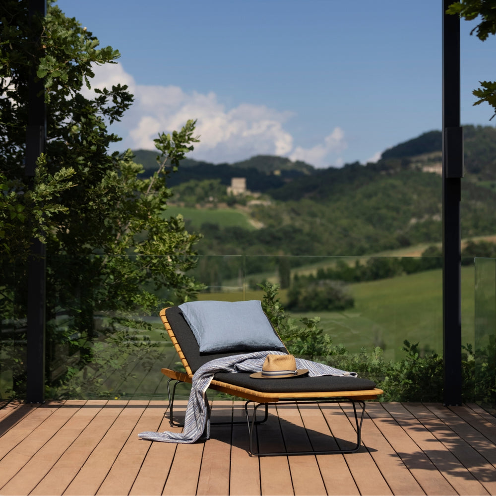 Pude fra HOUE i farven sky. Puden ses her i et udendørs billede på en loungeseng