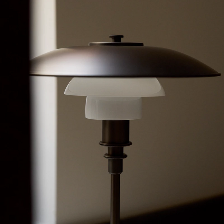 PH 3/2 Aged Brass Opal Bordlampe er en smuk nyhed fra Louis Poulsen, som har givet den klassiske lampe en ny smuk fortolkning med de brune farver.